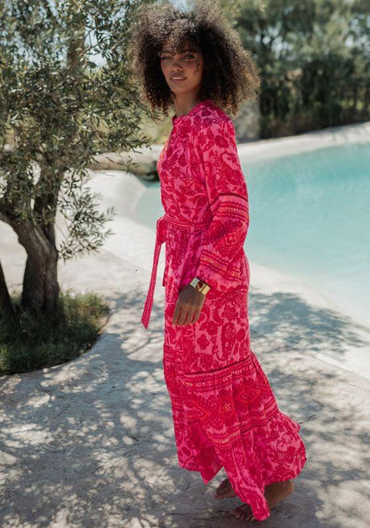 Samoa Dress Pink by Piti Cuiti, vibrant hot pink and red paisley beach dress with flowy sleeves and tiered skirt by the pool.
