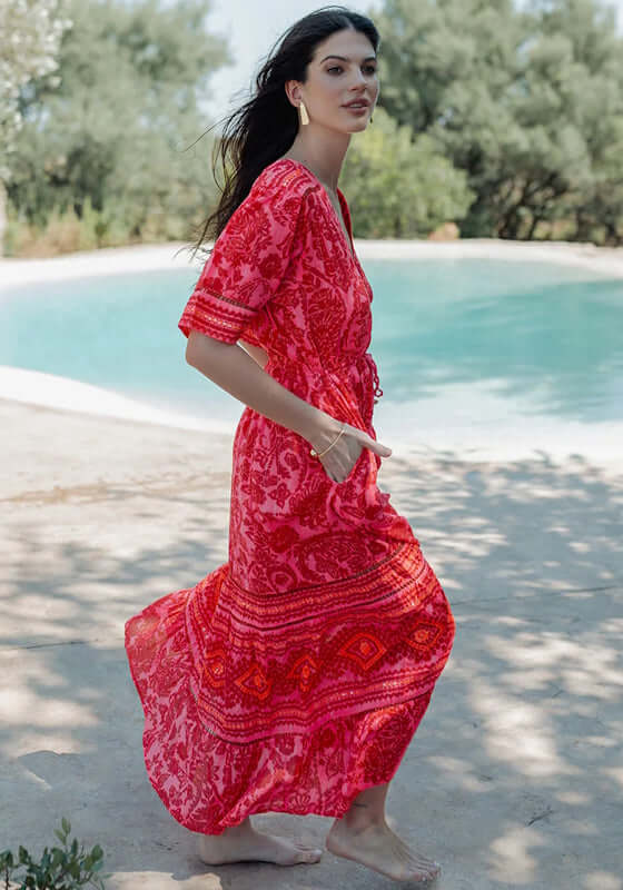 Samoa Short Sleeve Dress by Piti Cuiti worn outdoors, showcasing vibrant red and pink paisley fabric with a flowing maxi skirt.