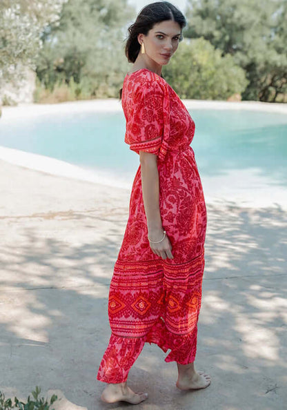 Samoa Short Sleeve Dress by Piti Cuiti worn by a model, showcasing vibrant red and pink paisley fabric by a pool.