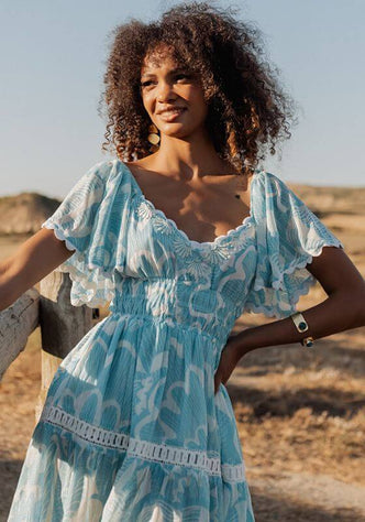 Shell Short Dress Blue by Piti Cuiti, a stylish blue beach dress with V neckline and tiered skirt in a natural setting.