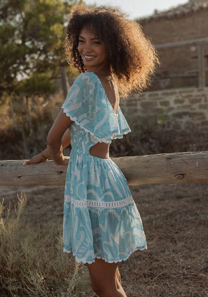 Shell Short Dress Blue by Piti Cuiti, showcasing the elegant V neckline and tiered skirt in a picturesque outdoor setting.