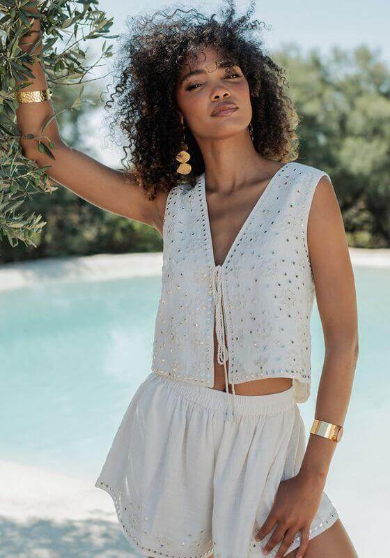 Sicilia Vest White by Piti Cuiti, a stylish tie-front design with mirrored details at a beach.