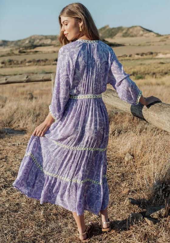 Sahara Purple Long Dress by Piti Cuiti, showcasing its flattering V neckline and tiered skirt against a scenic backdrop.