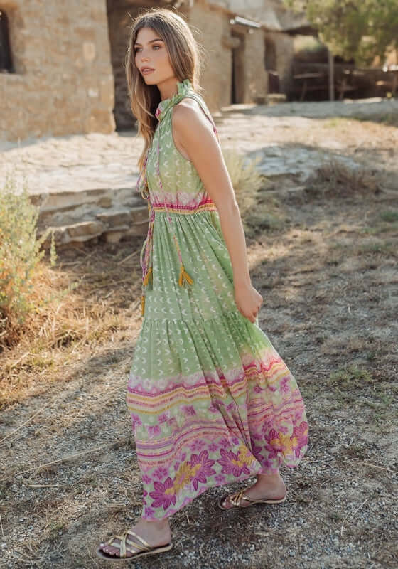 Curacao Dress Green by Piti Cuiti worn outdoors, showcasing a ruffled collar, tiered skirt, and playful tassels.