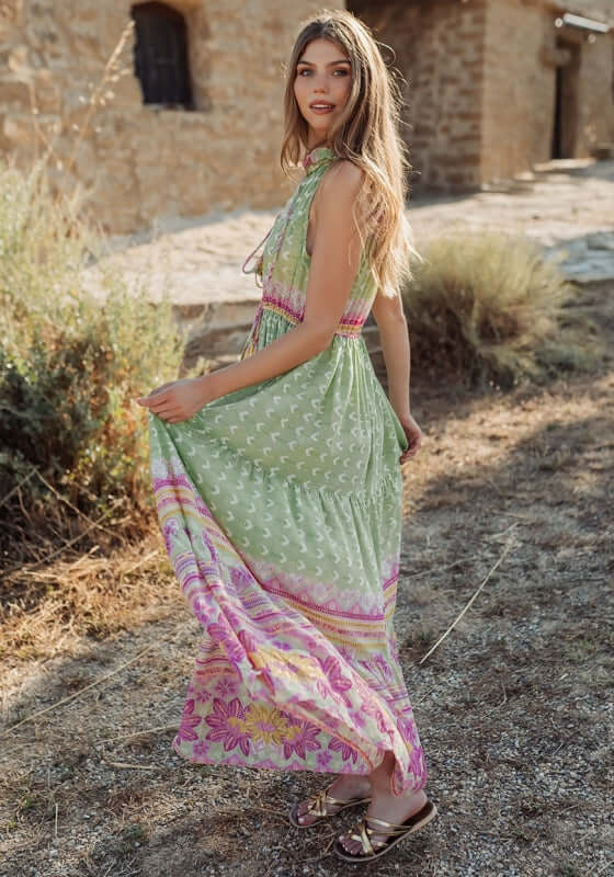 Curacao Dress Green by Piti Cuiti, a model twirls in a green and pink patterned resort-inspired maxi dress.