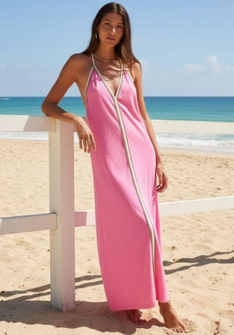 Pima Inca Dress Bubblegum by Pitusa, featuring a model in a pink dress on the beach with a serene ocean backdrop.