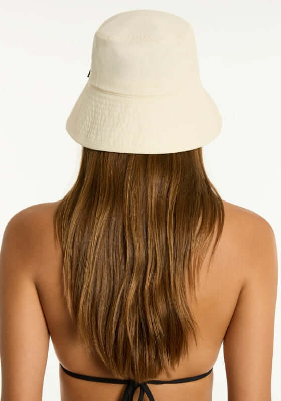 Canvas Bucket Beach Hat Ivory by Sea Level, featuring a stylish back view on a beach-ready model with long hair.
