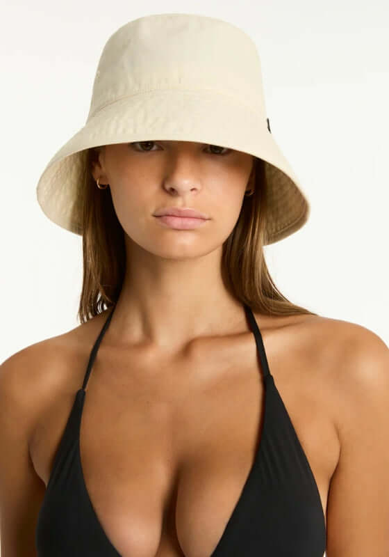 Canvas Bucket Beach Hat Ivory by Sea Level, model wearing a foldable ivory hat with a black bikini top.