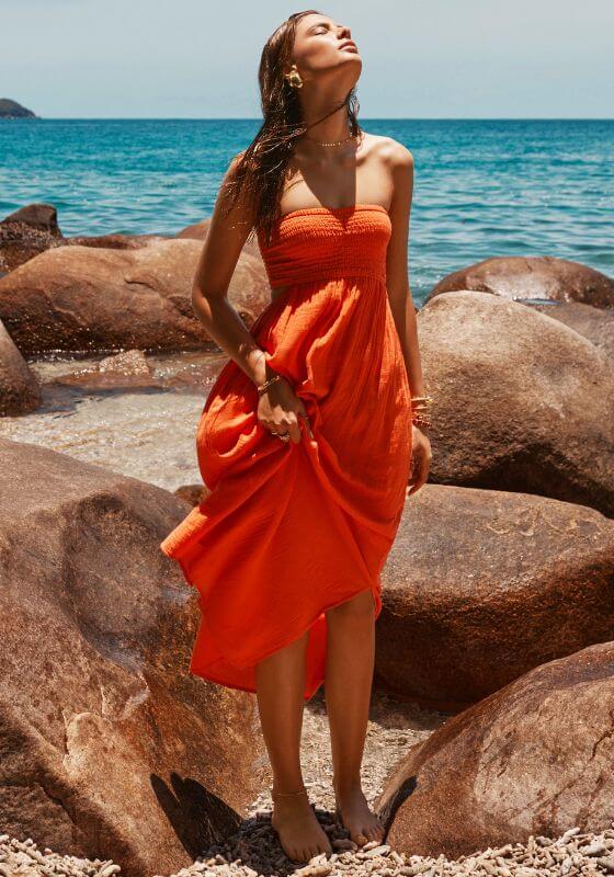 Sunset Bandeau Dress Flame by Sea Level, model wearing a red flame bandeau dress on a beach near the ocean.