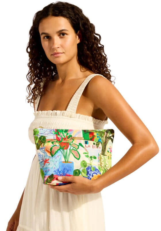 La Boca Beach Pouch by Seafolly, colorful beach pouch held by a model in a light dress.