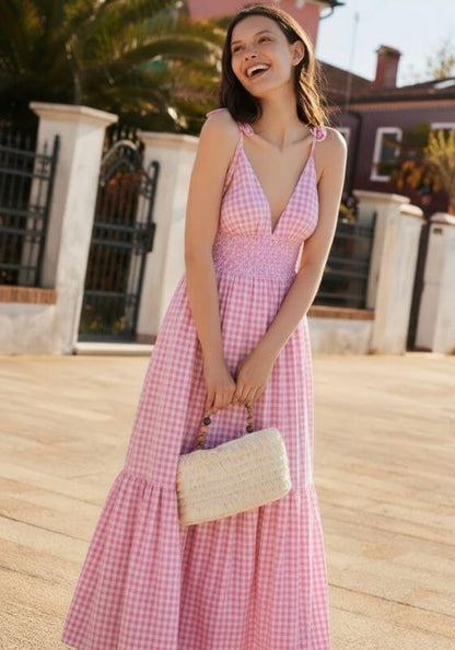 Yolanda Dress Pink Gingham by Sundress, a model wearing a pink gingham dress with an open back, smiling outdoors.