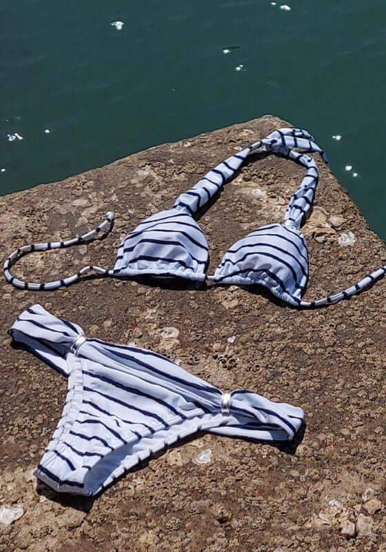 Bia Bikini Symphonie by Vix, navy and white striped bikini top and bottoms on a rock by the water.